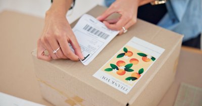 online-order-delivery-label-and-woman-hand-with-s-2025-04-05-14-56-42-utc shipping label being placed on box with branded sticker