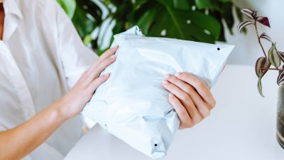 young red-haired attractive woman unpacking parcel at home hands holding a package in poly mailer